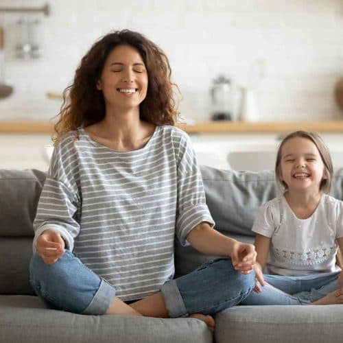 Mutter und Tochter meditieren gemeinsam zu Hause auf dem Sofa