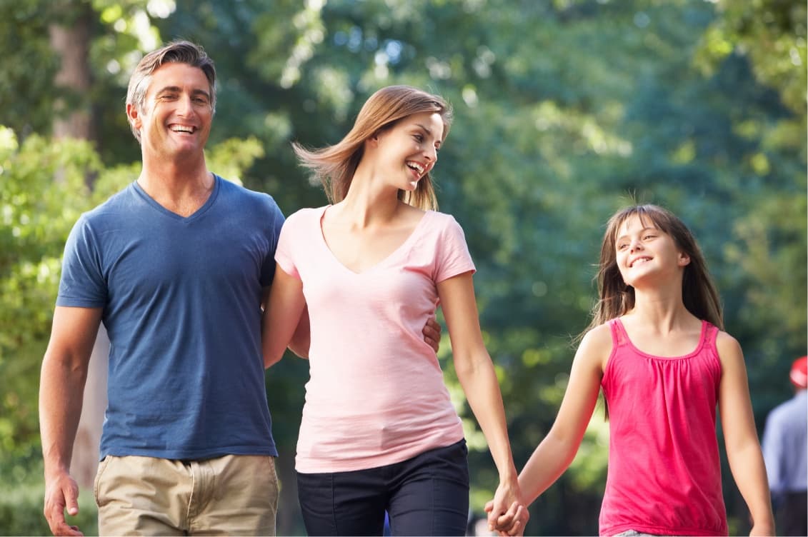 Eine Familie geht lächelnd durch einen sonnigen Park